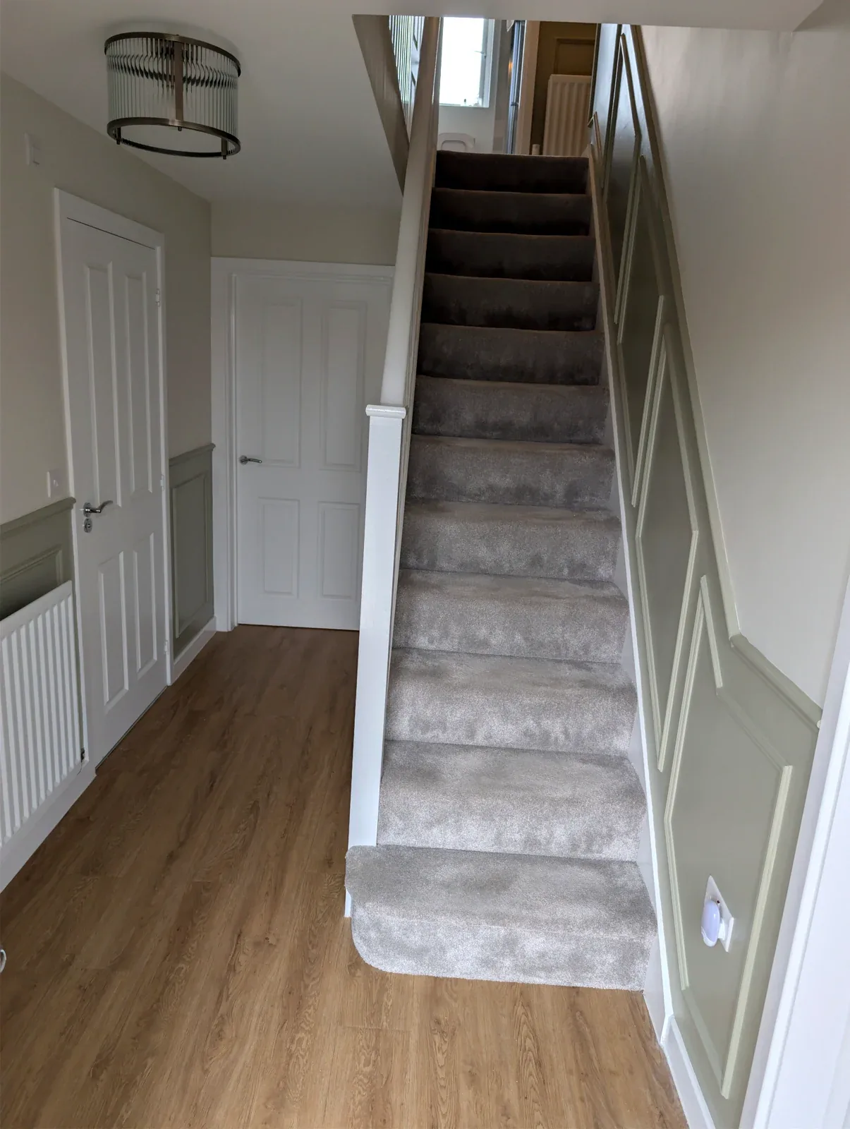 Light neutral hallway with painted wall mouldings and grey carpeted stairs
