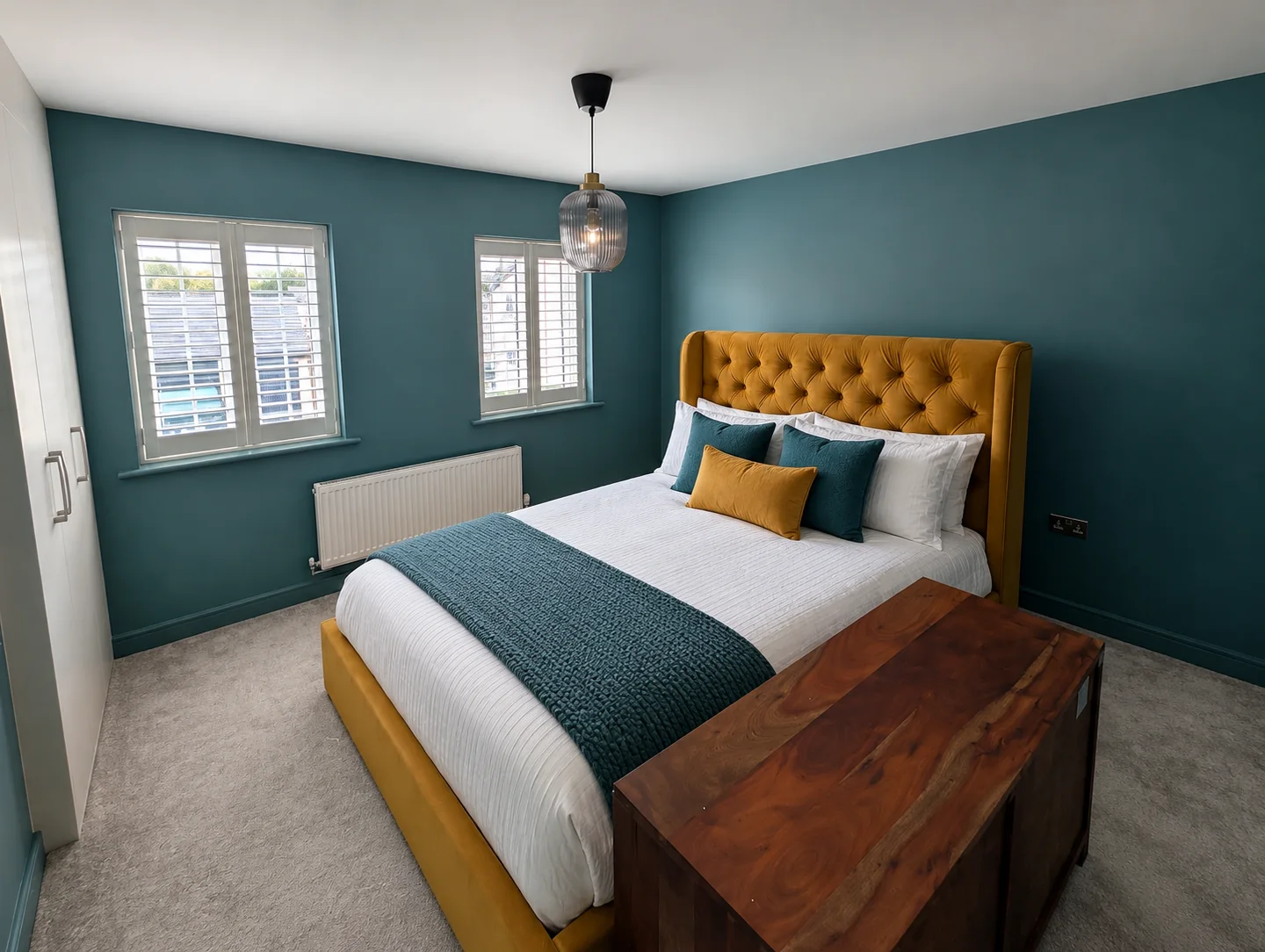 Teal-painted bedroom with a mustard headboard and white window shutters